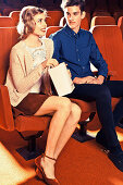 Junges Paar sitzt in einem Kinosaal und sie isst Popcorn