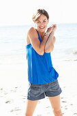 A mature brunette woman on a beach wearing a blue top and a silver bracelet