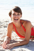 A mature brunette woman on a beach wearing a red bathing suit