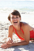 A mature brunette woman on a beach wearing a red bathing suit