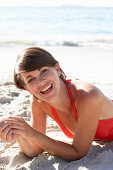 A mature brunette woman on a beach wearing a red bathing suit