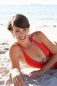 A mature brunette woman on a beach wearing a red bathing suit