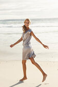 A mature blonde woman on a beach wearing a silver summer dress