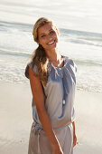 A mature blonde woman on a beach wearing a silver summer dress