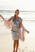 Reife blonde Frau mit silbernem Sommerkleid am Strand