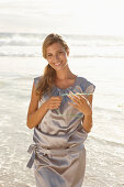 A mature blonde woman on a beach wearing a silver summer dres