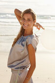 A mature blonde woman on a beach wearing a silver summer dress and holding a white balloon