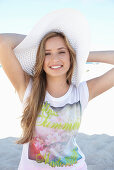 A young blonde woman on a beach wearing a colourful t-shirt and a white summer hat