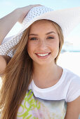 A young blonde woman on a beach wearing a colourful t-shirt and a white summer hat