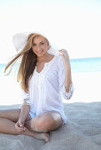 Junge blonde Frau in weißem Sommerkleid und weißem Sommerhut am Strand
