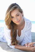 A young blonde woman on a beach wearing a white summer dress