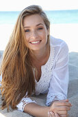 A young blonde woman on a beach wearing a white summer dress