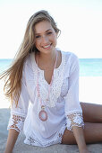 Junge blonde Frau in weißem Sommerkleid und pinker Halskette am Strand