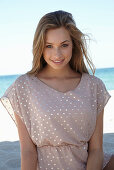 A young blonde woman on a beach wearing a beige polka-dot dress