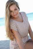 A young blonde woman on a beach wearing a beige polka-dot dress