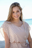 A young blonde woman on a beach wearing a beige polka-dot dress