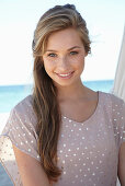 A young blonde woman on a beach wearing a beige polka-dot dress