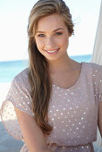 A young blonde woman on a beach wearing a beige polka-dot dress