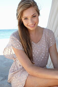 A young blonde woman on a beach wearing a beige polka-dot dress