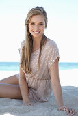 A young blonde woman on a beach wearing a beige polka-dot dress