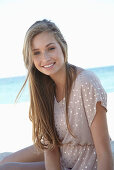 A young blonde woman on a beach wearing a beige polka-dot dress