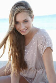 A young blonde woman on a beach wearing a beige polka-dot dress