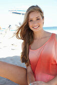 A young blonde woman on a beach wearing a salmon-coloured, off-the-shoulder top