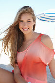 A young blonde woman on a beach wearing a salmon-coloured, off-the-shoulder top