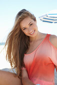 A young blonde woman on a beach wearing a salmon-coloured, off-the-shoulder top