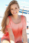 A young blonde woman on a beach wearing a salmon-coloured, off-the-shoulder top