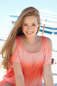 A young blonde woman on a beach wearing a salmon-coloured, off-the-shoulder top