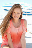 A young blonde woman on a beach wearing a salmon-coloured, off-the-shoulder top