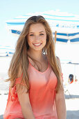 A young blonde woman on a beach wearing a salmon-coloured, off-the-shoulder top