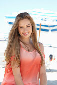 A young blonde woman on a beach wearing a salmon-coloured, off-the-shoulder top