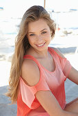 A young blonde woman on a beach wearing a salmon-coloured, off-the-shoulder top