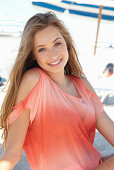 A young blonde woman on a beach wearing a salmon-coloured, off-the-shoulder top