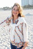 A brunette woman wearing a printed tunic and a white knitted jumper