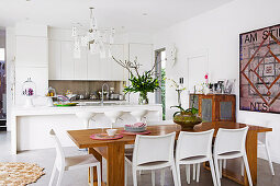 weiße Einbauküche mit Kücheninsel und Esstisch aus Holz mit weißen Stühlen