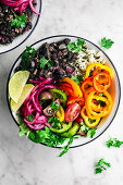 Vegan burrito bowls with spicy black beans, rice, summer vegetables, and pickled onons