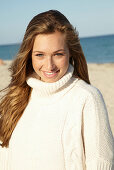 Junge blonde Frau in weißem Rollkragenpullover am Strand