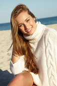 Junge blonde Frau in weißem Rollkragenpullover am Strand