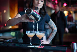 A bartender pouring cocktails into glasses