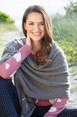 A brunette woman wearing a grey shawl and a pink knitted jumper with heats