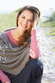 A brunette woman wearing a grey shawl and a pink knitted jumper with heats