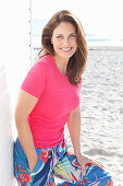 Brünette Frau in pinkfarbenem T-Shirt und bunter Hose am Strand