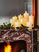 Christmas candles on mantelpiece with holly and open fire