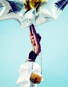 Junge Frau in weißem Rock und schwarz-weißem Top mit goldenen und silbernen Luftballons