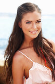 A young brunette woman with hair extensions by the sea wearing a pink top