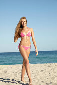 Junge blonde Frau im rosa Bikini am Meer