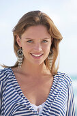 A young brunette woman on a beach wearing a black-and-white striped top